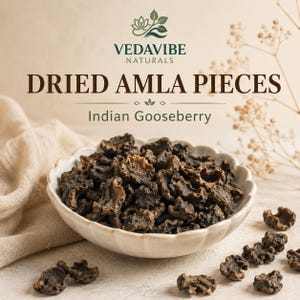Puede incluir: Un cuenco blanco festoneado lleno de trozos de amla secos de color marrón oscuro y arrugados, también conocidos como grosella espinosa india. El texto VEDAVIBE NATURALS, DRIED AMLA PIECES e Indian Gooseberry aparece sobre el cuenco.