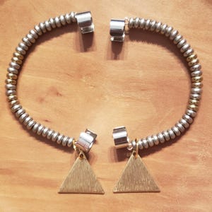 May include: A pair of hoop earrings featuring a series of small, alternating silver and gold-toned metallic beads strung on a wire. Each earring is finished with a polished silver-toned clasp at the top and a flat, brushed gold-toned triangle charm.