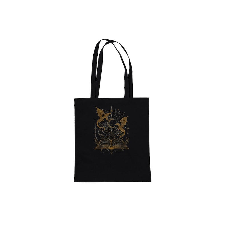 A black fabric tote bag with short handles displays a central gold graphic of a magical book and dragons against a plain white background.