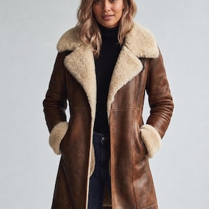 May include: A brown long-length coat with a distressed leather finish, featuring a wide cream-colored shearling collar and matching shearling cuffs. The coat has a straight-cut silhouette, visible vertical seam detailing, and an open front design.