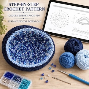 May include: A crochet project featuring a bowl filled with blue and clear beads, accompanied by three yarn balls in shades of blue, a crochet hook, a needle, a bead organizer, and a tablet displaying a STEP-BY-STEP CROCHET PATTERN GEODE SENSORY ROCK PDF.