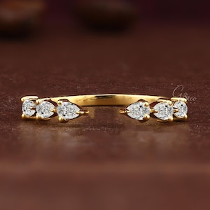 May include: A gold open-style ring featuring six pear-cut white stones set in a row, with three stones on each side of the opening. The band is polished yellow gold, and the stones are arranged symmetrically to create a delicate, continuous appearance.