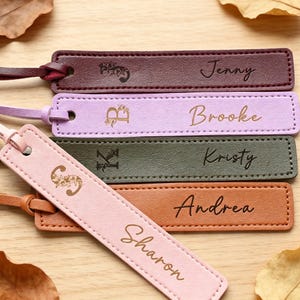Puede incluir: Cinco marcapáginas rectangulares de cuero con bordes cosidos y borlas de cuero a juego. Cada marcapáginas presenta una inicial adornada con flores y un nombre grabado en cursiva: Jenny, Brooke, Kristy, Andrea y Sharon en varios colores.