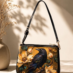 Può includere: Una borsa a spalla nera con corpo rettangolare e stampa raffigurante un corvo scuro appollaiato tra grandi fiori giallo pallido su sfondo marrone dorato. La borsa presenta un sottile cinturino nero e una chiusura superiore con cerniera.