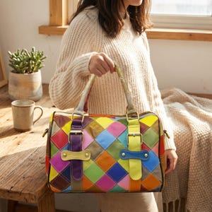 Puede incluir: Un bolso con un diseño de patchwork multicolor con paneles de cuero en forma de diamante en tonos rojo, amarillo, azul, verde, morado y naranja. El bolso incluye dos correas verticales con hebillas metálicas y detalles en tono dorado.