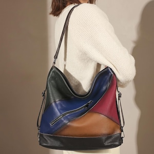 Può includere: Una borsa a tracolla in pelle multicolore con un design patchwork. La borsa presenta pannelli verdi, blu, bordeaux, marroni e neri. Ha una chiusura con cerniera e una lunga tracolla.