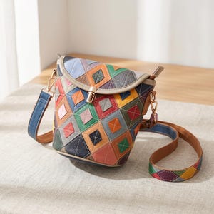Peut inclure: Un sac bandoulière de forme seau avec un motif patchwork en losanges multicolores dans des tons bleu, vert, orange, rouge, jaune et gris. Le sac présente une fermeture à verrou tournant en métal doré sur le rabat et une bandoulière assortie.