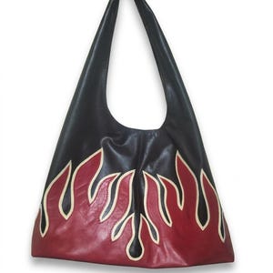Peut inclure: Un sac à bandoulière noir de style hobo orné d'un motif de flammes sur la partie inférieure. Les flammes sont représentées en rouge foncé avec des contours passepoilés couleur crème, contrastant avec le corps en cuir noir du sac.