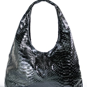 May include: Black leather hobo bag with a textured, snakeskin-like pattern. The bag has a single shoulder strap and a rounded shape. The glossy finish reflects light, highlighting the intricate details of the material. The bag is set against a white background.