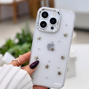 May include: Clear phone case with silver star and dot embellishments. The case has a silver camera ring and the Apple logo. The text "cepoyna" is printed on the bottom right corner of the case.