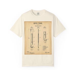 Op de afbeelding: Een crèmekleurig t-shirt met een vintage patentillustratie van een bijenkorfgereedschap. De afbeelding toont drie aanzichten gelabeld Fig. 1, Fig. 2 en Fig. 3, met technische labels, afmetingen in inches en de tekst Hive Tool Patent No. 445,789.