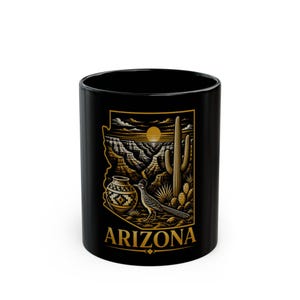 Può includere: Una tazza in ceramica nera con una grafica color oro e marrone dello stato dell'Arizona. Il design include un paesaggio desertico con un cactus saguaro, un roadrunner, un vaso di terracotta decorato e un canyon sotto un sole, con il testo ARIZONA.
