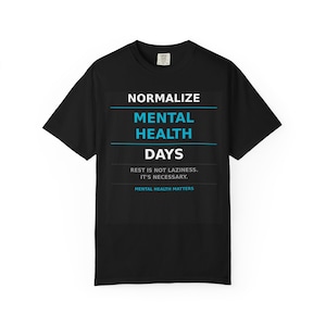Puede incluir: Una camiseta negra de manga corta con texto en blanco y azul claro que dice NORMALIZE MENTAL HEALTH DAYS, REST IS NOT LAZINESS. IT'S NECESSARY., y MENTAL HEALTH MATTERS, con líneas horizontales que separan las frases en la parte frontal.
