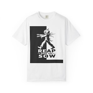 May include: A white short-sleeve t-shirt featuring a black and white graphic of a pumpkin-headed figure walking. The design is set against a split black and white background with the text REAP WHAT YOU SOW printed in bold black capital letters.