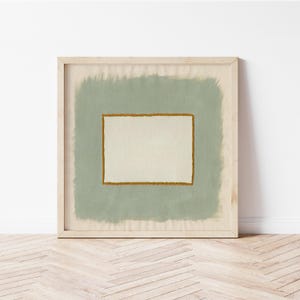 May include: A square framed wall art piece featuring a central off-white rectangular area bordered by a textured mustard-yellow line, set against a sage-green painted background with visible brushstroke edges, all enclosed in a light wood frame.