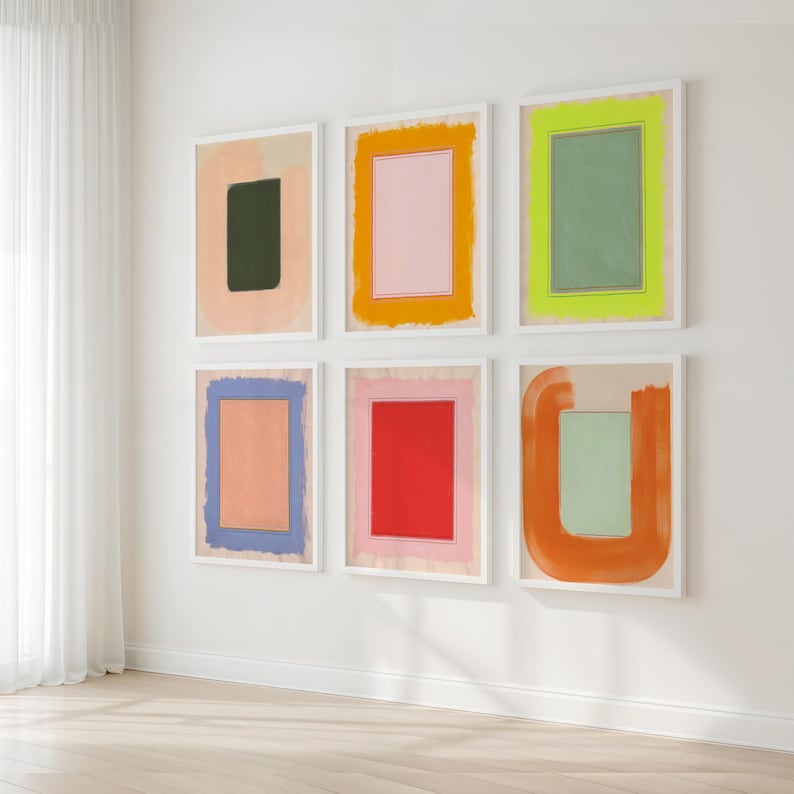 May include: Six framed abstract art prints with colorful geometric shapes. The artwork features a variety of colors, including pink, orange, green, blue, and red, with white frames. The art is displayed on a white wall.