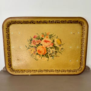 May include: A rectangular mustard yellow serving tray featuring a central floral bouquet with pink, orange, and white flowers. The border is decorated with a dark brown vine and leaf pattern, and the surface includes eight small white circular accents.