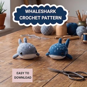 May include: Two crocheted whale shark toys, one gray and one blue, sit on a wooden surface. The blue whale shark has white spots. The image includes text that reads "WHALESHARK CROCHET PATTERN" and "EASY TO DOWNLOAD".