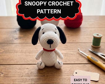 Puede incluir: Un perro Snoopy de ganchillo, blanco con orejas y nariz negras, y un collar rojo, está sentado sobre una superficie de madera. La imagen presenta el texto "Snoopy Crochet Pattern" y "Easy to Download".