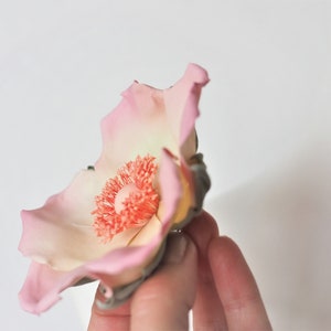 May include: A delicate pink and white flower with a bright orange center. The flower is made of fondant and is perfect for decorating cakes or cupcakes.
