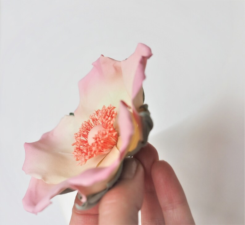 May include: A delicate pink and white flower with a bright orange center. The flower is made of fondant and is perfect for decorating cakes or cupcakes.
