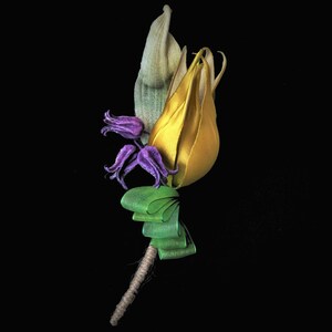 May include: A handcrafted floral boutonniere featuring a yellow tulip, purple flowers, and green ribbon accents. The stem is wrapped in twine, creating a rustic yet elegant look. Perfect for weddings or special occasions.