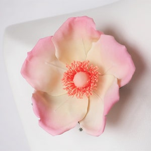 May include: A delicate pink and white flower with a coral center. The flower is made of fabric and has a realistic appearance.