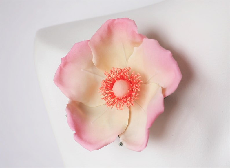 May include: A delicate pink and white flower with a coral center. The flower is made of fabric and has a realistic appearance.