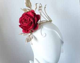 May include: A headpiece featuring a large, vibrant red rose centered on one side, accented by metallic gold leaves and thin, curved gold wire stems topped with small gold beads, all mounted on a structured, thin gold-toned wire frame base.