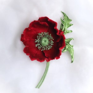 May include: A red velvet poppy flower with green leaves and stem. The flower is a handmade craft item.