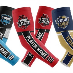 Pode incluir: Três pares de mangas desportivas em preto e azul, vermelho, e azul-marinho e dourado. Cada manga apresenta um gráfico de escudo com o texto YOUR LOGO no topo e uma faixa preta vertical exibindo texto personalizado como YOUR NAME, PLAYER NAME ou TEAM NAME.