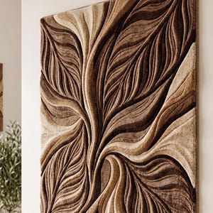 May include: A rectangular wall hanging featuring a textured, three-dimensional surface with deep, flowing grooves. The design consists of layered, organic wave patterns in varying shades of brown, tan, and cream, creating a sculpted effect.