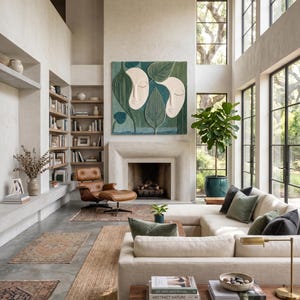 May include: A large square wall art piece featuring two stylized cream-colored faces surrounded by textured green leaves in various shades. The artwork is mounted above a fireplace in a room with high ceilings, a beige sofa, and wooden shelves.