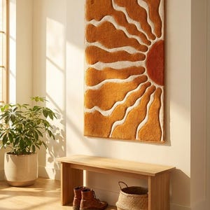 Könnte beinhalten: Ein rechteckiger Wandbehang mit einem getufteten Sonnenstrahlen-Motiv in gebranntem Orange und Creme. Das strukturierte Textilkunstwerk zeigt eine große halbkreisförmige Sonne auf der rechten Seite mit strahlenden, wellenförmigen Strahlen.