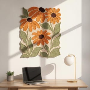 May include: A rectangular tufted wall hanging featuring three large orange flowers with dark brown centers and textured green leaves on a cream-colored background. The piece has an irregular, wavy edge and a thick, soft, yarn-like pile texture.