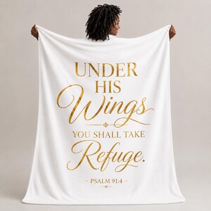 May include: A white throw blanket featuring gold metallic text that reads: UNDER HIS Wings YOU SHALL TAKE Refuge. PSALM 91:4. The design includes a small decorative star-like symbol above and below the scripture reference, centered on the fabric.