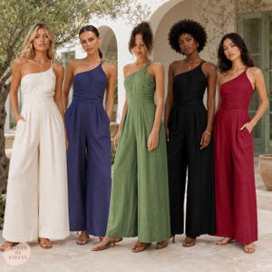 May include: Five one-shoulder jumpsuits in cream, navy blue, olive green, black, and deep red. Each jumpsuit features a fitted bodice with a defined waistline, wide-leg trousers with side pockets, and a textured fabric finish. Woven by Evelyn logo.