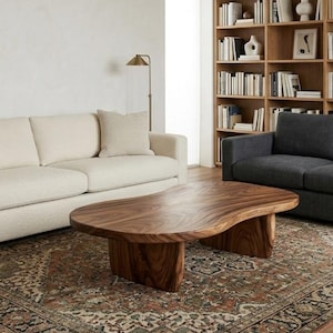 May include: A low-profile coffee table crafted from solid wood with a natural grain pattern, featuring an organic, kidney-shaped top and two thick, curved slab legs that provide a sturdy base for the smooth, polished surface of the table.