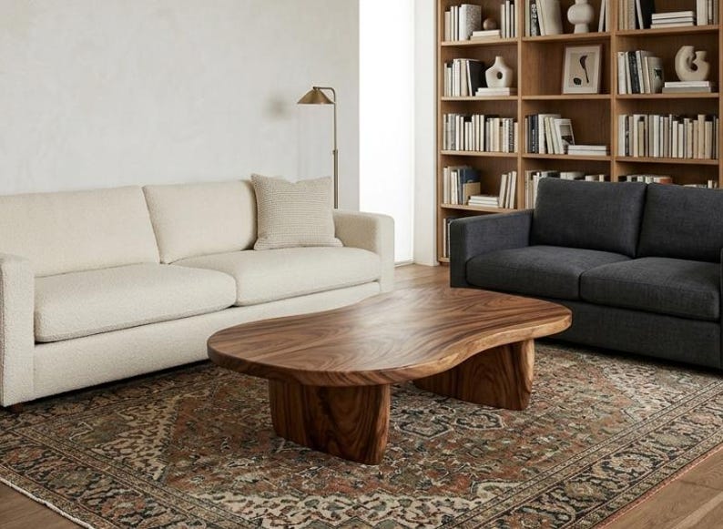 May include: A low-profile coffee table crafted from solid wood with a natural grain pattern, featuring an organic, kidney-shaped top and two thick, curved slab legs that provide a sturdy base for the smooth, polished surface of the table.