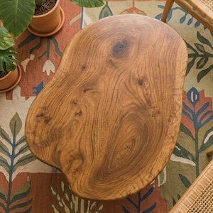 May include: A coffee table with an irregular, organic shape crafted from natural wood. The surface displays a prominent grain pattern with visible knots and swirls in warm brown tones. The edges are smooth and rounded, following the natural contour of the wood slab, creating a distinct, non-geometric silhouette that serves as a central piece of furniture.