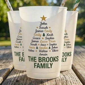 May include: Three frosted plastic cups with paper straws, each featuring a printed Christmas tree design composed of various names in gold and green text, topped with a gold star, and the phrase THE BROOKS FAMILY printed at the base.