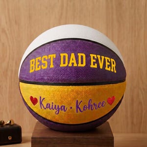 May include: A basketball featuring a white top panel, a purple middle panel with the yellow text BEST DAD EVER, and a yellow bottom panel. The bottom panel displays the purple text Kaiya &bull; Kohree flanked by two small red heart icons.