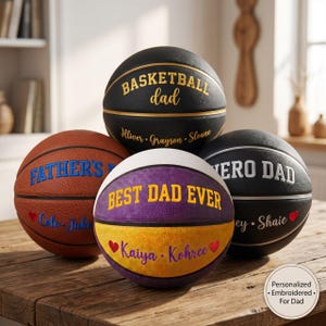 May include: Four basketballs with personalized text. One black ball says BASKETBALL dad with names. One brown ball says FATHER'S DAY with names and a red heart. One purple and yellow ball says BEST DAD EVER with names and red hearts. One black ball says HERO DAD.