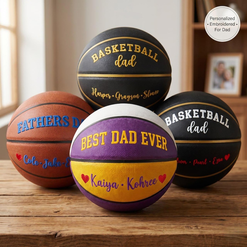 May include: Four basketballs with personalized embroidery. One is brown with blue text, one is black with gold text, one is black with white text, and one is purple and yellow with yellow text. Each ball features names and phrases like Basketball Dad.