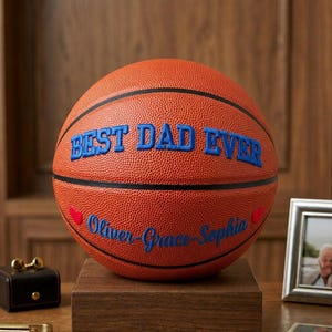 May include: An orange basketball with black seams featuring the blue text BEST DAD EVER in a bold font. Below the text, the names Oliver, Grace, and Sophia are printed in blue script, flanked by two small red hearts on the textured surface.