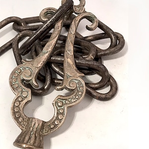 May include: A silver and brass chain with a decorative, ornate, and intricately designed end piece. The chain is made of metal links and the end piece is shaped like a flower with a small hole in the centre.