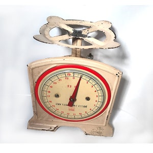 May include: A vintage white kitchen scale with a red dial and black markings. The scale reads up to 22 pounds and has the text "Not Legal For Trade" printed on the dial.