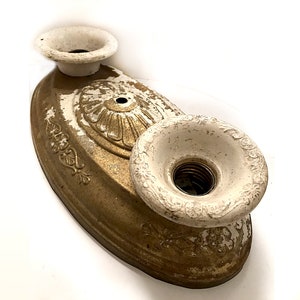 May include: A vintage gold-coloured metal ceiling fixture with two white porcelain sockets. The fixture has a decorative design with floral motifs.