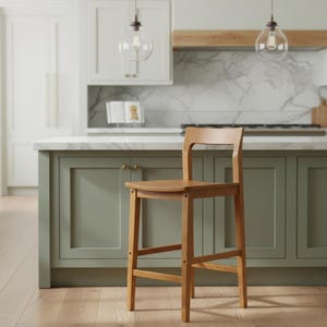 May include: A light brown wooden bar stool with a square seat, a low backrest, and four straight legs connected by horizontal support bars on all sides. The stool features a smooth, natural wood grain finish and a simple, functional design.