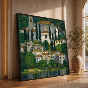 May include: A framed rectangular wall art print depicting a hillside village with stone buildings, tall cypress trees, and lush green foliage overlooking a dark blue body of water, rendered in a textured, impressionistic painting style.